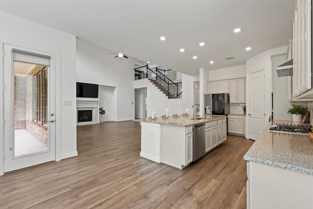 kitchen with light stone countertops, stainless steel appliances, a center island with sink, light hardwood / wood-style floors, and white cabinetry