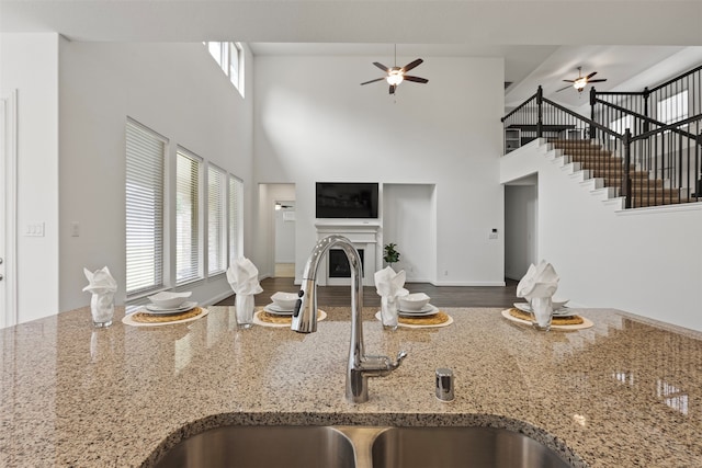 kitchen featuring a high ceiling, sink, ceiling fan, light stone counters, and wood-type flooring