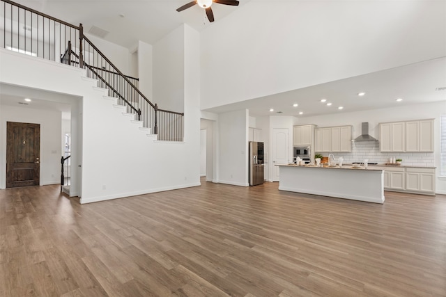 unfurnished living room featuring light wood-type flooring, a towering ceiling, and ceiling fan