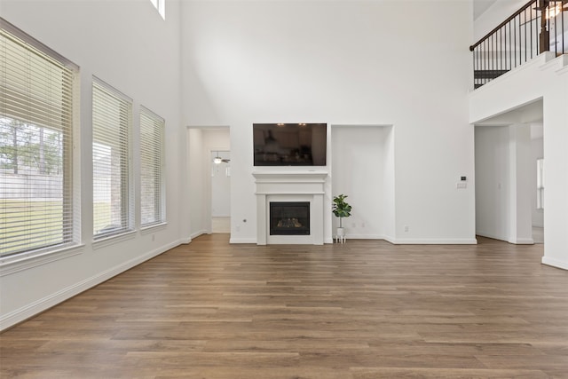 unfurnished living room featuring a towering ceiling, hardwood / wood-style flooring, and ceiling fan