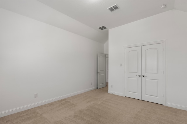 unfurnished bedroom featuring light carpet, vaulted ceiling, and a closet