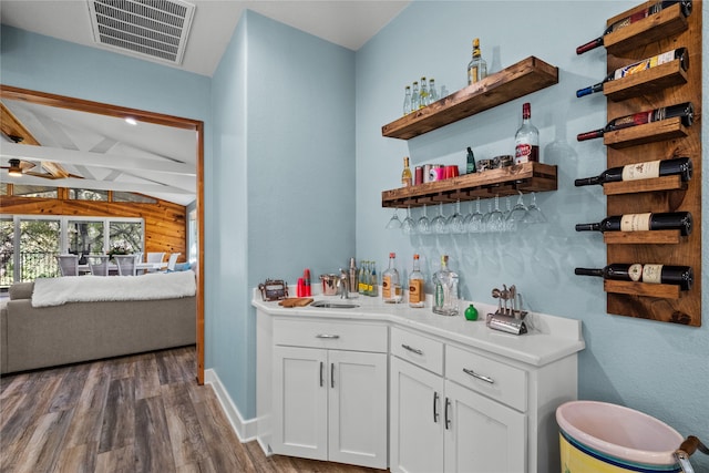 bar with white cabinetry, dark hardwood / wood-style flooring, wooden walls, and vaulted ceiling