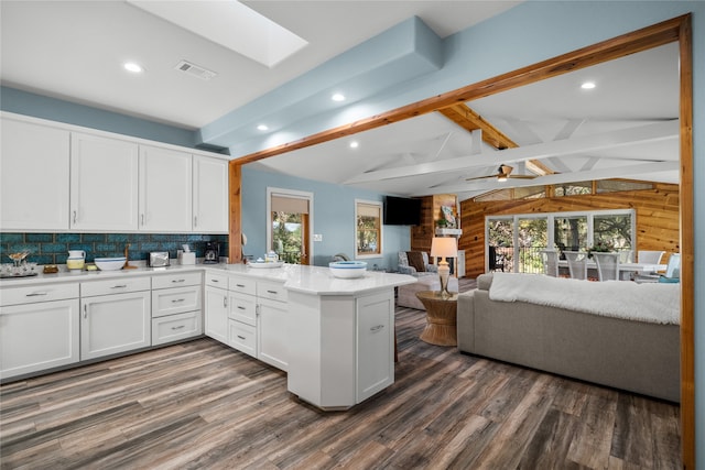 kitchen featuring vaulted ceiling with skylight, dark hardwood / wood-style floors, white cabinets, kitchen peninsula, and ceiling fan