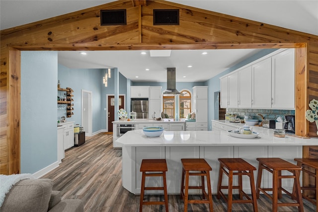 kitchen with stainless steel appliances, white cabinetry, kitchen peninsula, island exhaust hood, and dark hardwood / wood-style flooring