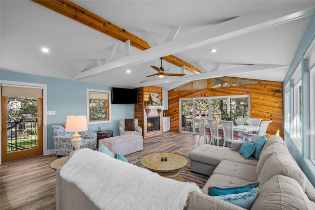 living room featuring wood walls, a wealth of natural light, wood-type flooring, and vaulted ceiling with beams