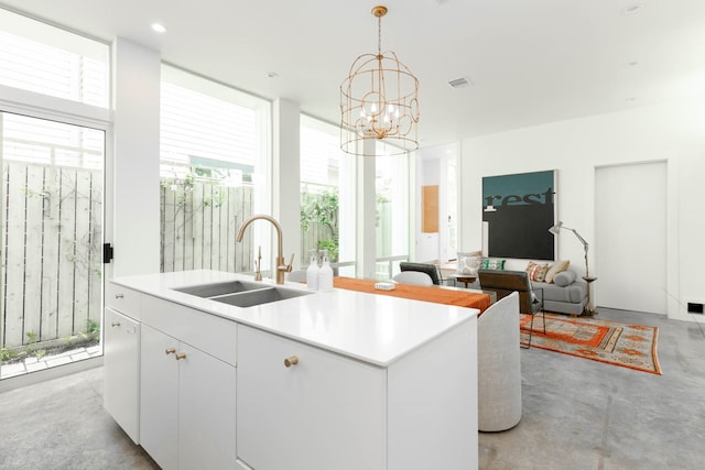 kitchen featuring a center island with sink, sink, white cabinetry, an inviting chandelier, and hanging light fixtures