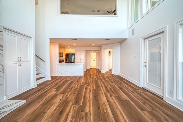 unfurnished living room featuring dark wood-type flooring and a towering ceiling