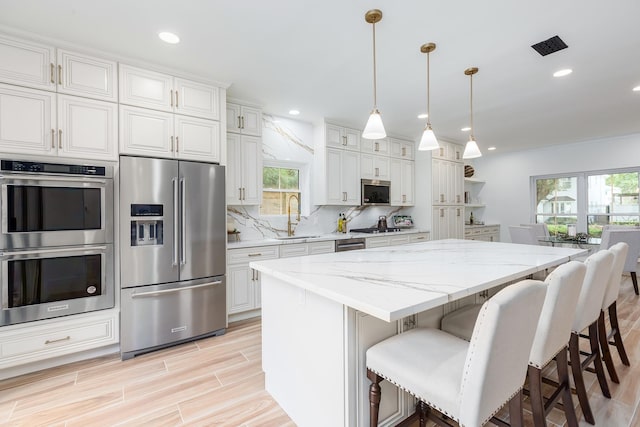 kitchen featuring stainless steel appliances, hanging light fixtures, a center island, light stone counters, and sink