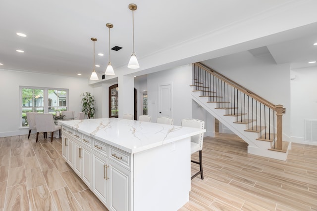 kitchen featuring a breakfast bar, light stone counters, a kitchen island, pendant lighting, and white cabinets