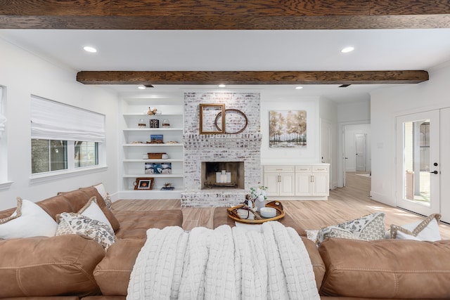 living room with built in shelves, beam ceiling, light hardwood / wood-style floors, and a brick fireplace