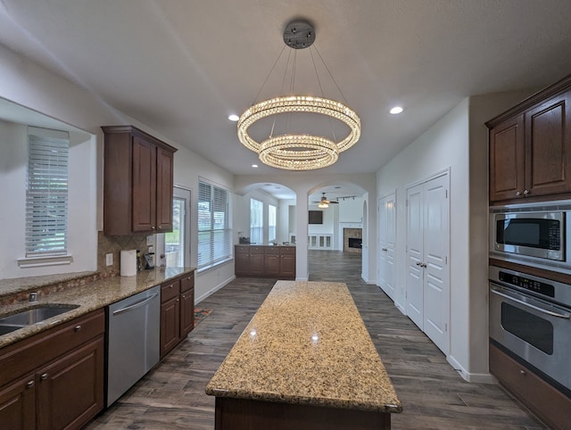 kitchen with dark wood-type flooring, a kitchen island, decorative light fixtures, and stainless steel appliances