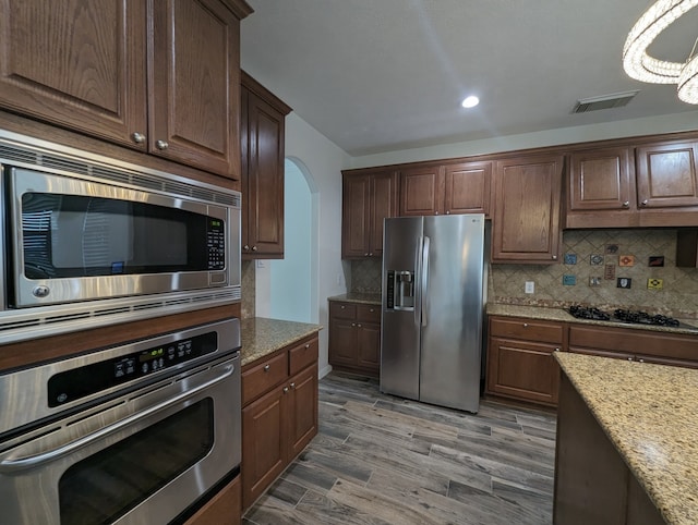 kitchen featuring stainless steel appliances, wood-type flooring, light stone counters, dark brown cabinetry, and tasteful backsplash