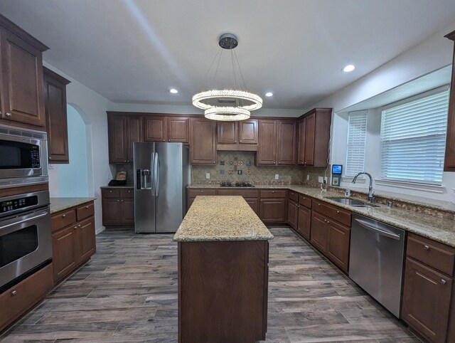 kitchen with stainless steel appliances, decorative light fixtures, sink, hardwood / wood-style flooring, and a center island