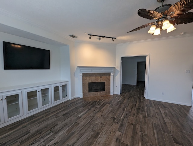 unfurnished living room with ceiling fan, a tiled fireplace, dark hardwood / wood-style flooring, and ornamental molding