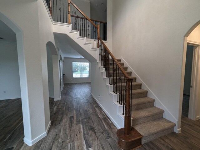 stairway with wood-type flooring and a towering ceiling