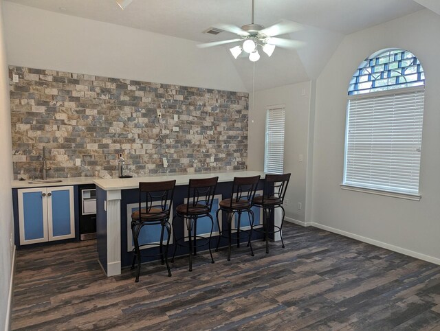 interior space with dark hardwood / wood-style floors, ceiling fan, vaulted ceiling, and a breakfast bar area