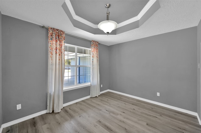 spare room featuring light wood-type flooring, ornamental molding, and a raised ceiling