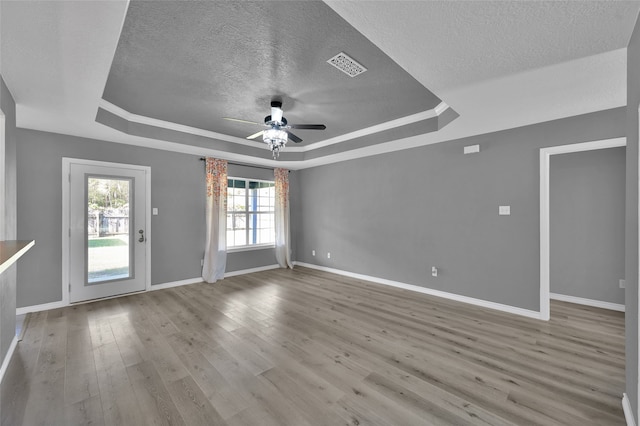 unfurnished room with light wood-type flooring, a textured ceiling, ceiling fan, and a raised ceiling