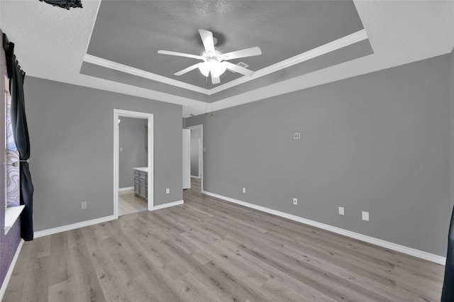 unfurnished bedroom featuring ensuite bathroom, a tray ceiling, ceiling fan, and light hardwood / wood-style flooring