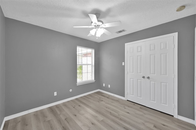 unfurnished bedroom with a closet, a textured ceiling, ceiling fan, and light hardwood / wood-style flooring