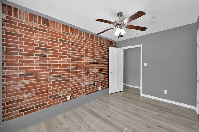 unfurnished room featuring light wood-type flooring, brick wall, and ceiling fan