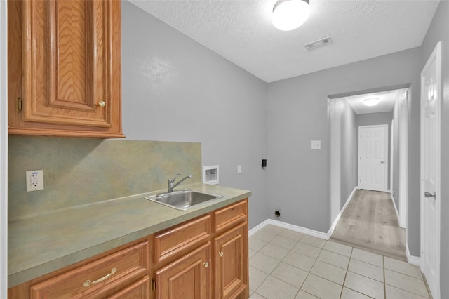 washroom with light tile patterned flooring, hookup for an electric dryer, hookup for a washing machine, a textured ceiling, and sink