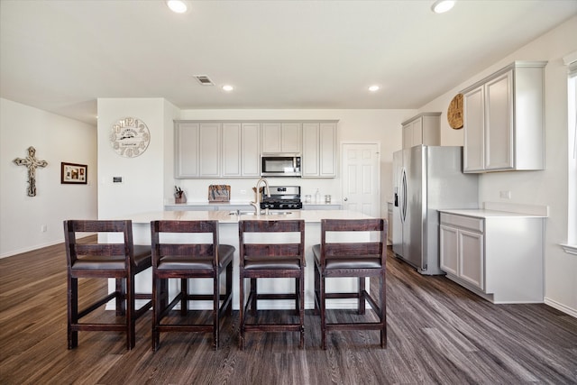 kitchen featuring appliances with stainless steel finishes, a kitchen island with sink, sink, dark hardwood / wood-style floors, and a breakfast bar area