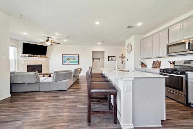 kitchen with sink, stainless steel appliances, dark hardwood / wood-style floors, an island with sink, and a fireplace