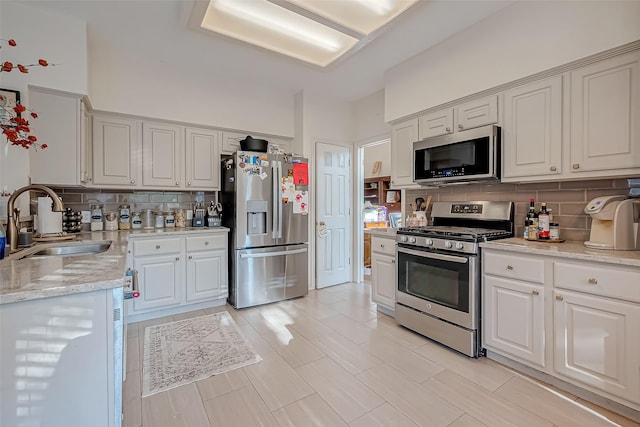 kitchen with decorative backsplash, sink, light stone counters, and appliances with stainless steel finishes