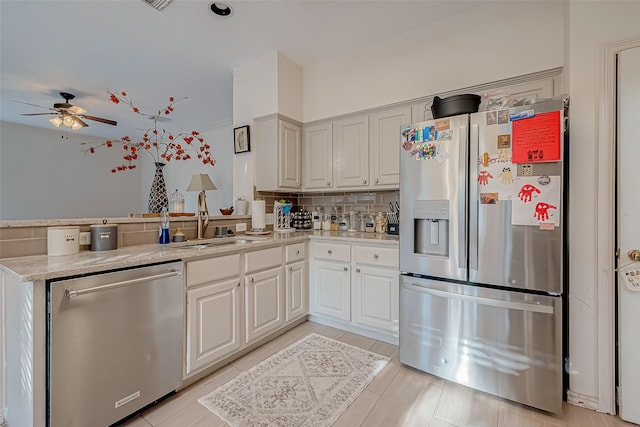 kitchen with white cabinets, stainless steel appliances, decorative backsplash, sink, and ceiling fan