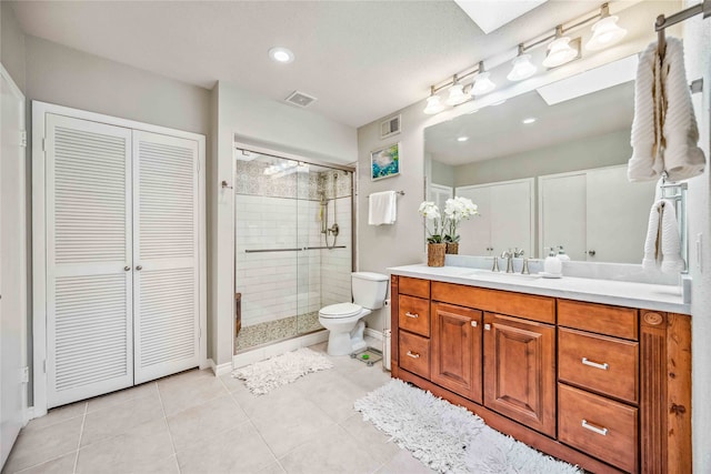 bathroom with tile patterned flooring, a skylight, vanity, a shower with shower door, and toilet