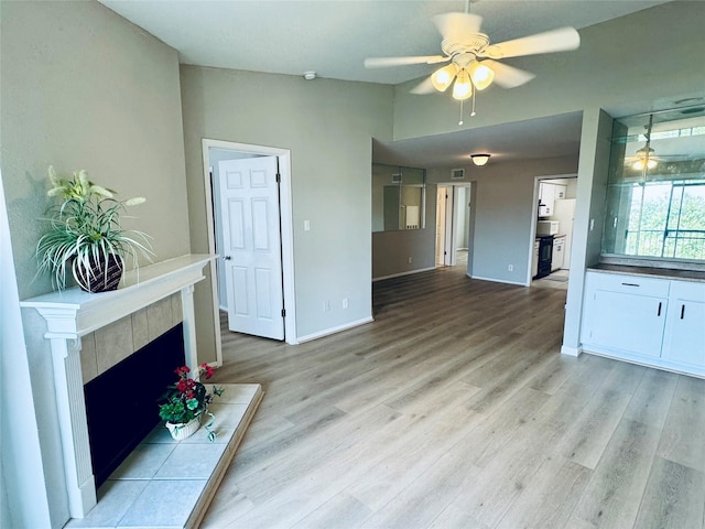 unfurnished living room with a tiled fireplace, light hardwood / wood-style flooring, and ceiling fan