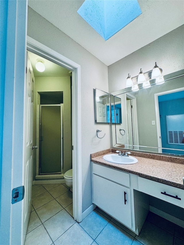 bathroom featuring a shower with door, a skylight, vanity, tile patterned floors, and toilet