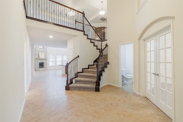 entrance foyer featuring french doors, a towering ceiling, and a fireplace