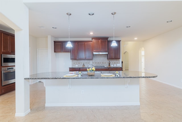 kitchen with dark stone counters, decorative light fixtures, a kitchen island with sink, and stainless steel appliances