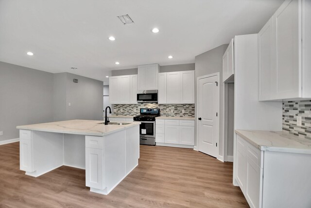 kitchen with stainless steel appliances, light stone countertops, light hardwood / wood-style floors, white cabinets, and a kitchen island with sink