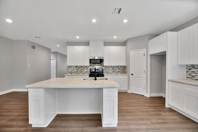 kitchen featuring wood-type flooring, a kitchen island with sink, light stone counters, and white cabinets