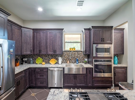 kitchen featuring decorative backsplash, stainless steel appliances, sink, and light stone countertops