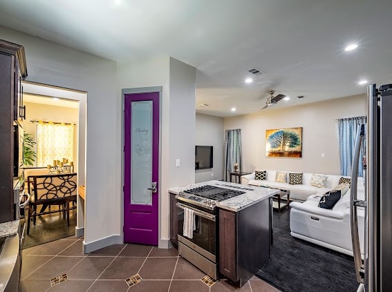 kitchen with light stone countertops, dark brown cabinets, dark tile patterned floors, and appliances with stainless steel finishes