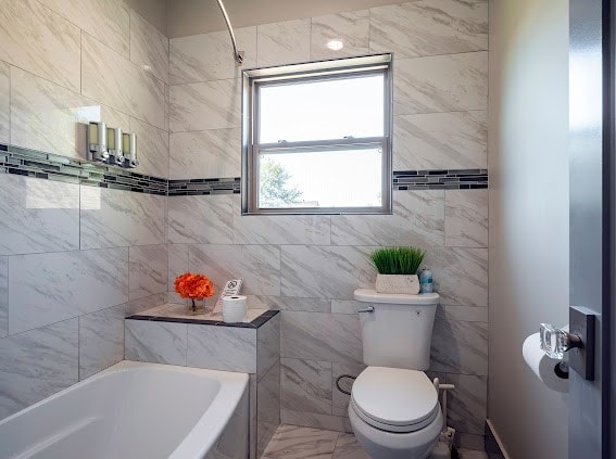 bathroom with toilet, tile walls, and tiled shower / bath combo