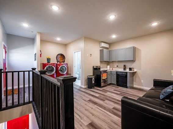 kitchen featuring an AC wall unit, black dishwasher, gray cabinets, stainless steel range, and light hardwood / wood-style flooring