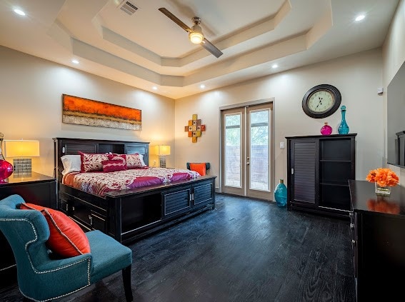 bedroom featuring french doors, dark hardwood / wood-style flooring, access to exterior, ceiling fan, and a raised ceiling