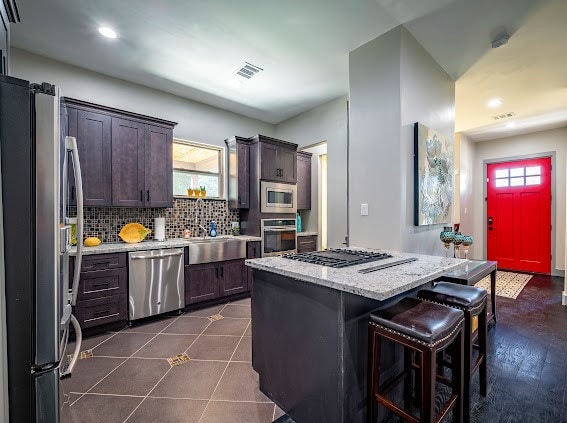 kitchen featuring decorative backsplash, dark brown cabinetry, a kitchen island, a breakfast bar, and appliances with stainless steel finishes