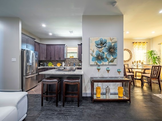 kitchen with dark hardwood / wood-style flooring, a breakfast bar area, stainless steel fridge with ice dispenser, backsplash, and dark brown cabinets