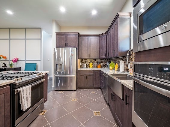 kitchen featuring tasteful backsplash, light stone countertops, appliances with stainless steel finishes, and dark brown cabinetry