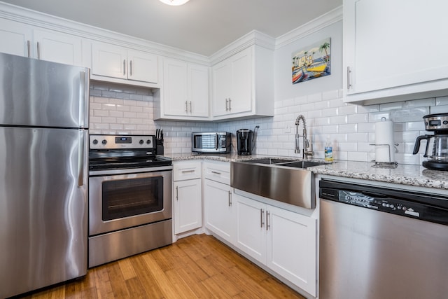 kitchen featuring white cabinets, light wood-type flooring, stainless steel appliances, and crown molding