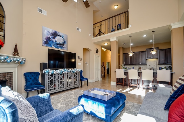 living room with a high ceiling, a tile fireplace, and ceiling fan