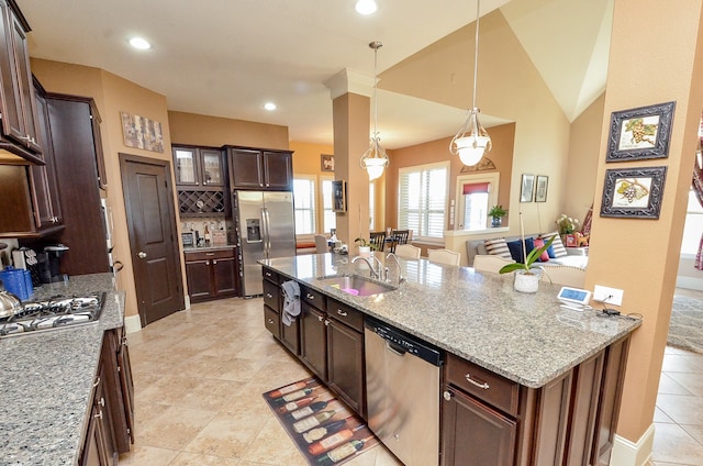 kitchen featuring light stone counters, stainless steel appliances, decorative light fixtures, sink, and lofted ceiling