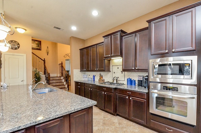 kitchen featuring stainless steel appliances, dark brown cabinets, light stone countertops, hanging light fixtures, and sink