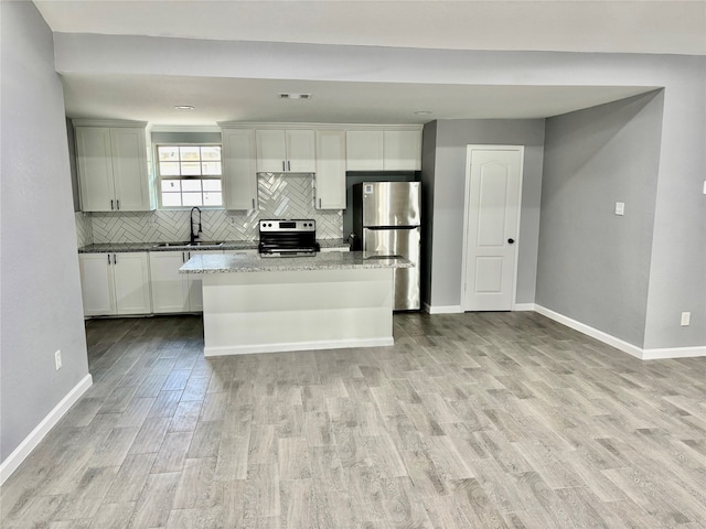 kitchen featuring light hardwood / wood-style floors, sink, appliances with stainless steel finishes, dark stone countertops, and a kitchen island